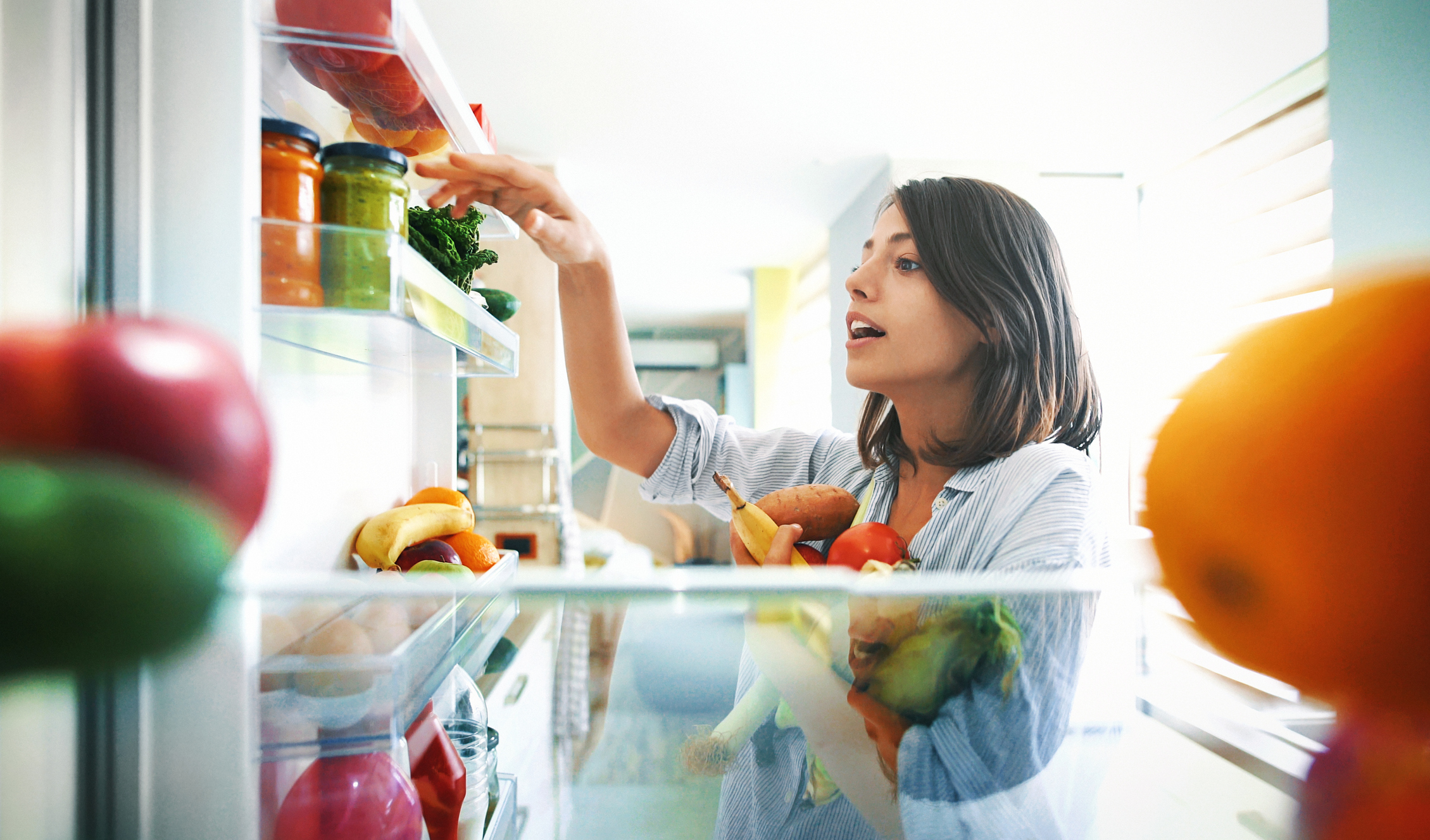 周日早晨，一对快乐的年轻夫妇从冰箱里挑选一些水果和蔬菜来做一些健康的早餐。这是从冰箱里拍摄的。