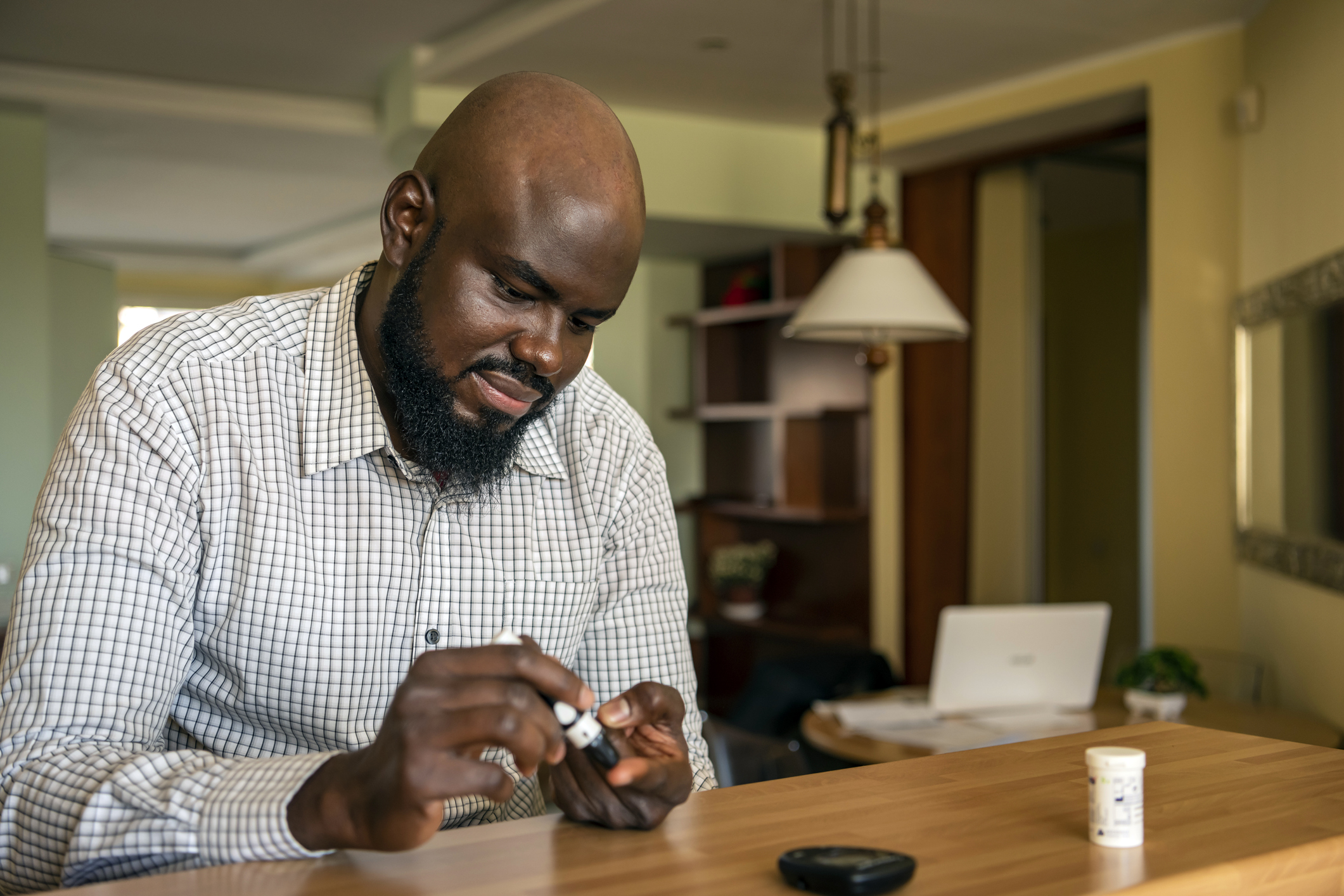 一名现代非裔商人正坐在家中办公室的办公桌前，从手指上取血，因为他患有糖尿病。一位患有慢性疾病、正在使用血糖仪的非裔美国人的日常生活。