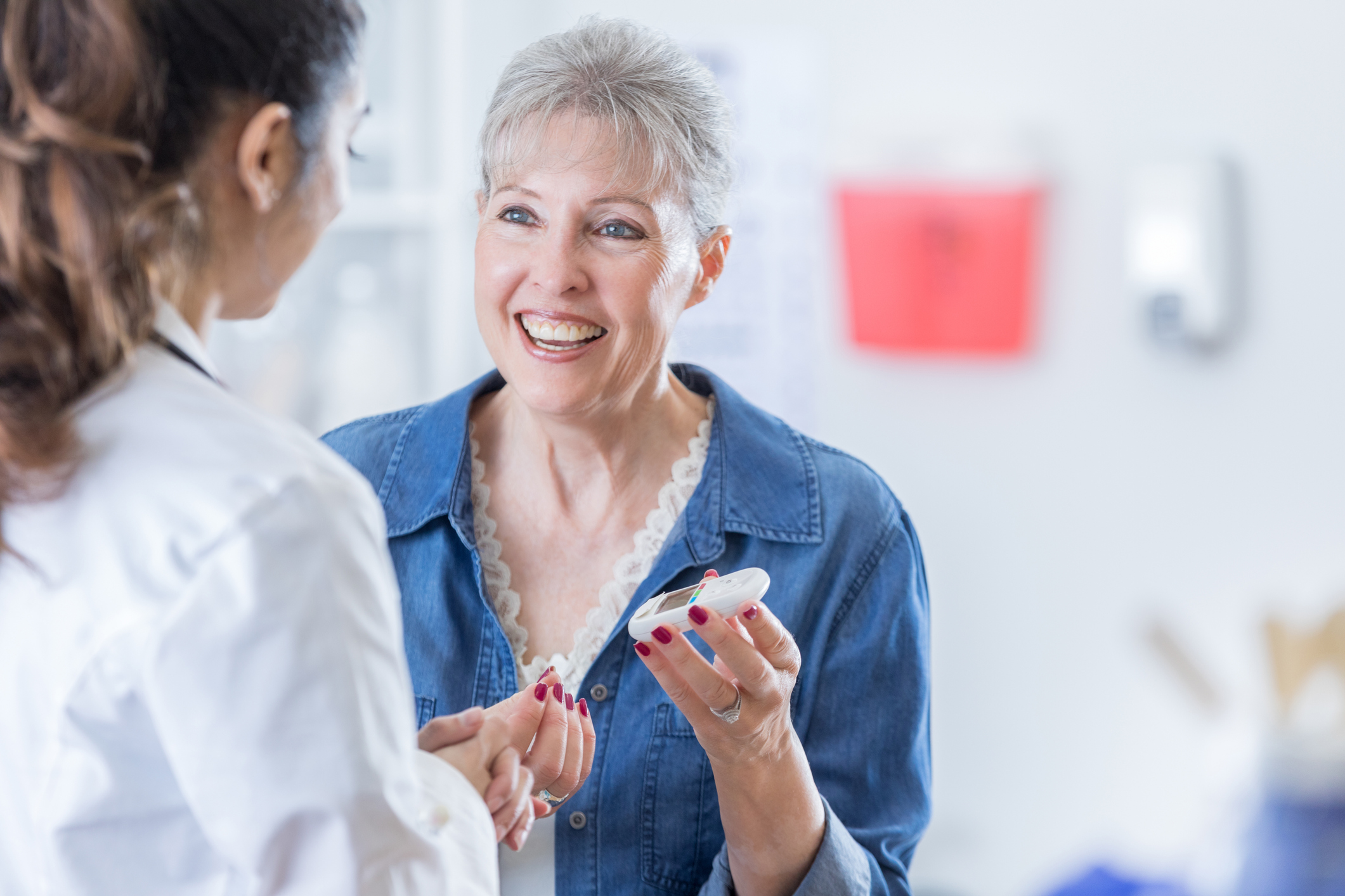 一位面带微笑的老年女性拿着一个血糖仪检查她的血糖水平。她正在和她的医生谈话。