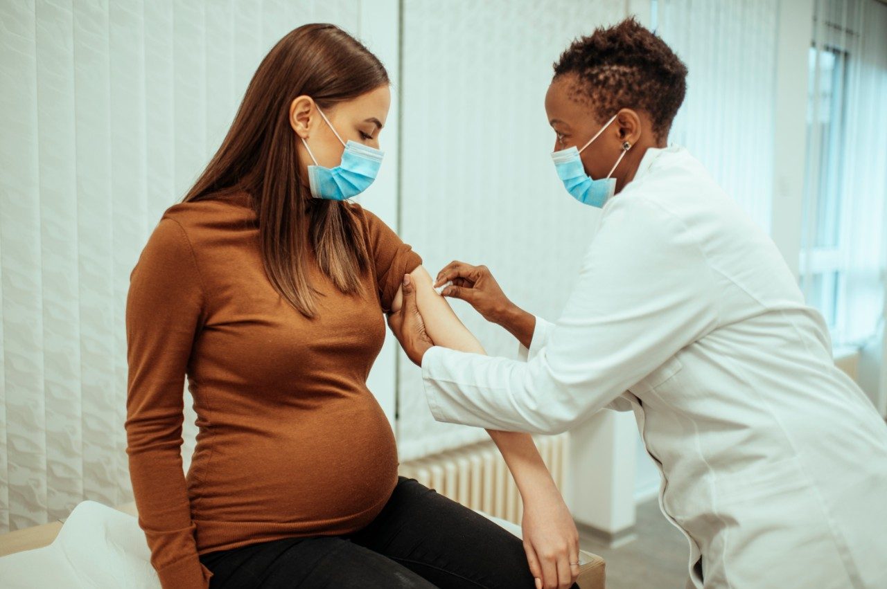 非裔美国女医生让一名孕妇准备好接种疫苗。孕妇接种 COVID-19 疫苗。