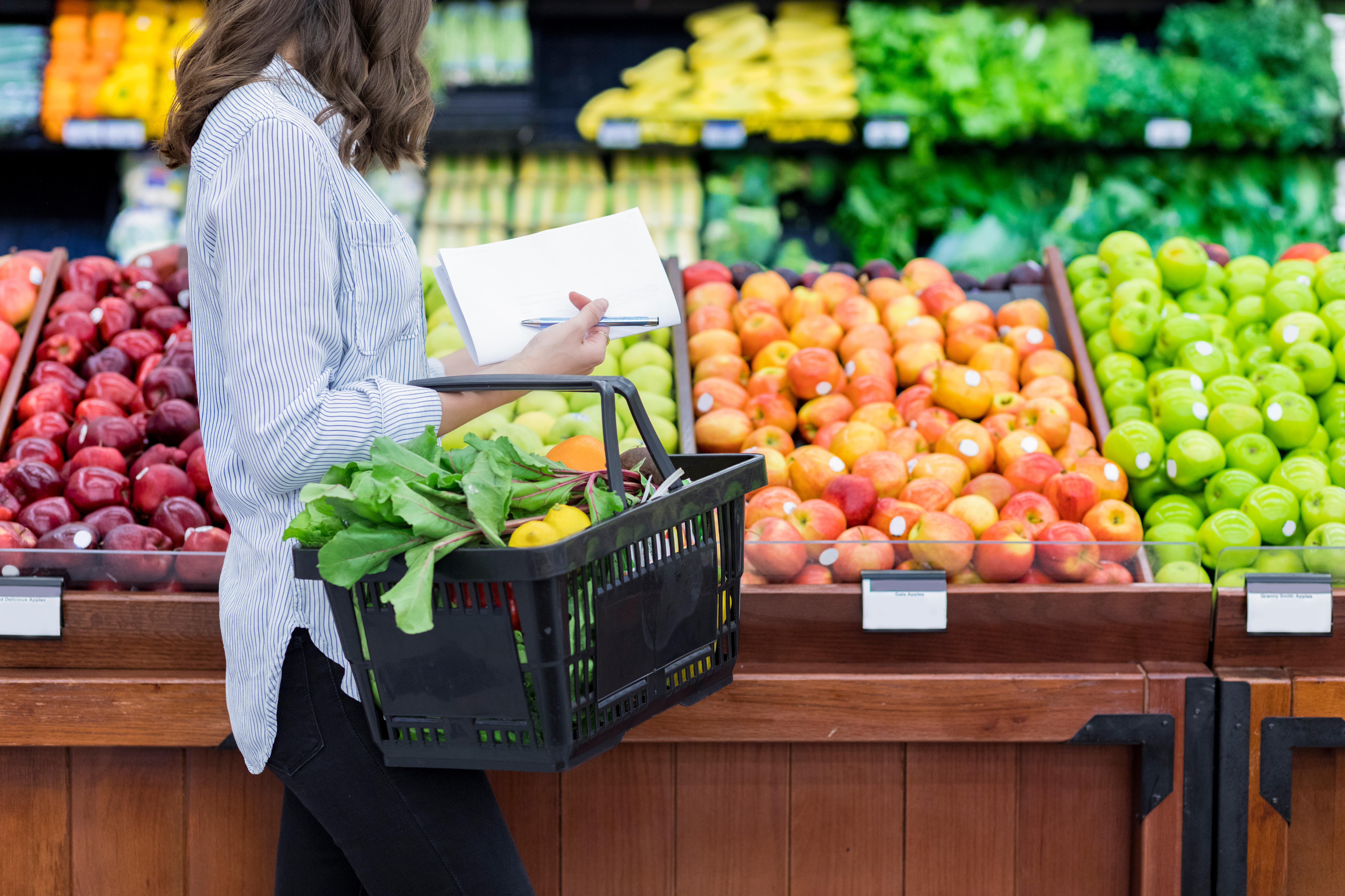 年轻女性携带一个装满新鲜农产品的购物篮。她在一家杂货店里买新鲜水果和蔬菜。