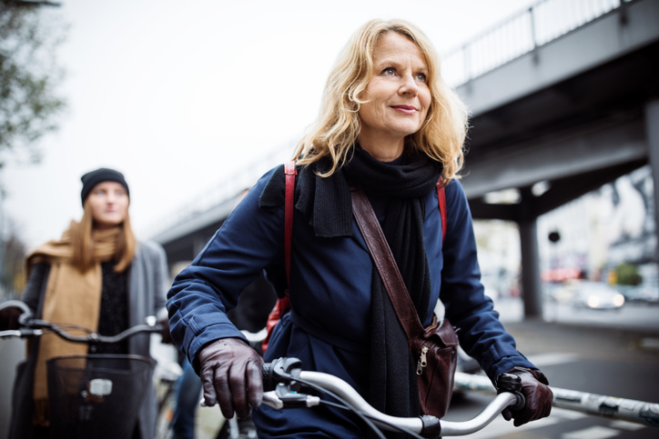 微笑着骑自行车的成熟女性。一起在城市旅行的朋友。他们穿着暖和的衣服。