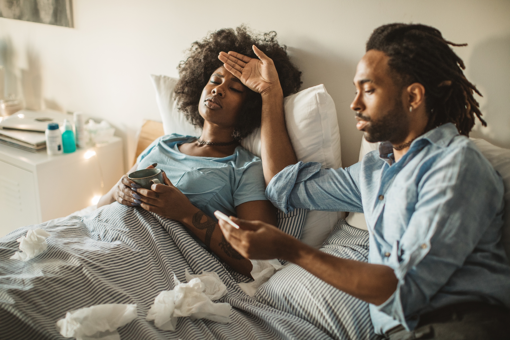 年轻的非洲裔美国女性在家里感到不舒服。躺在床上，喝茶，吃药。她的男朋友或丈夫照顾她。白天。
