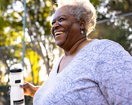 一位面带微笑的年长女性在阳光明媚的公园里喝水