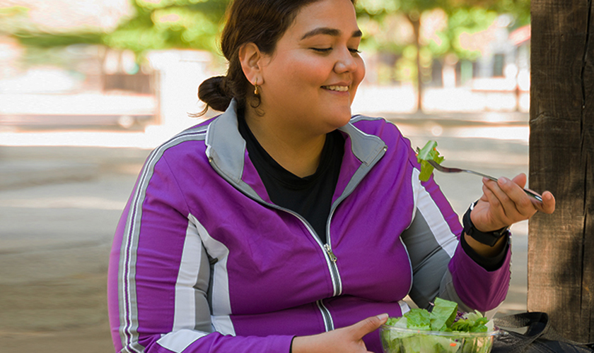 在开始户外有氧运动前，一位快乐的超重女性微笑着吃着健康的绿色沙拉