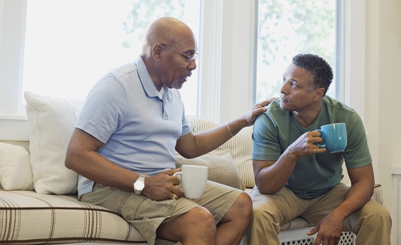 年长的父亲和儿子在沙发上边喝咖啡边交谈。